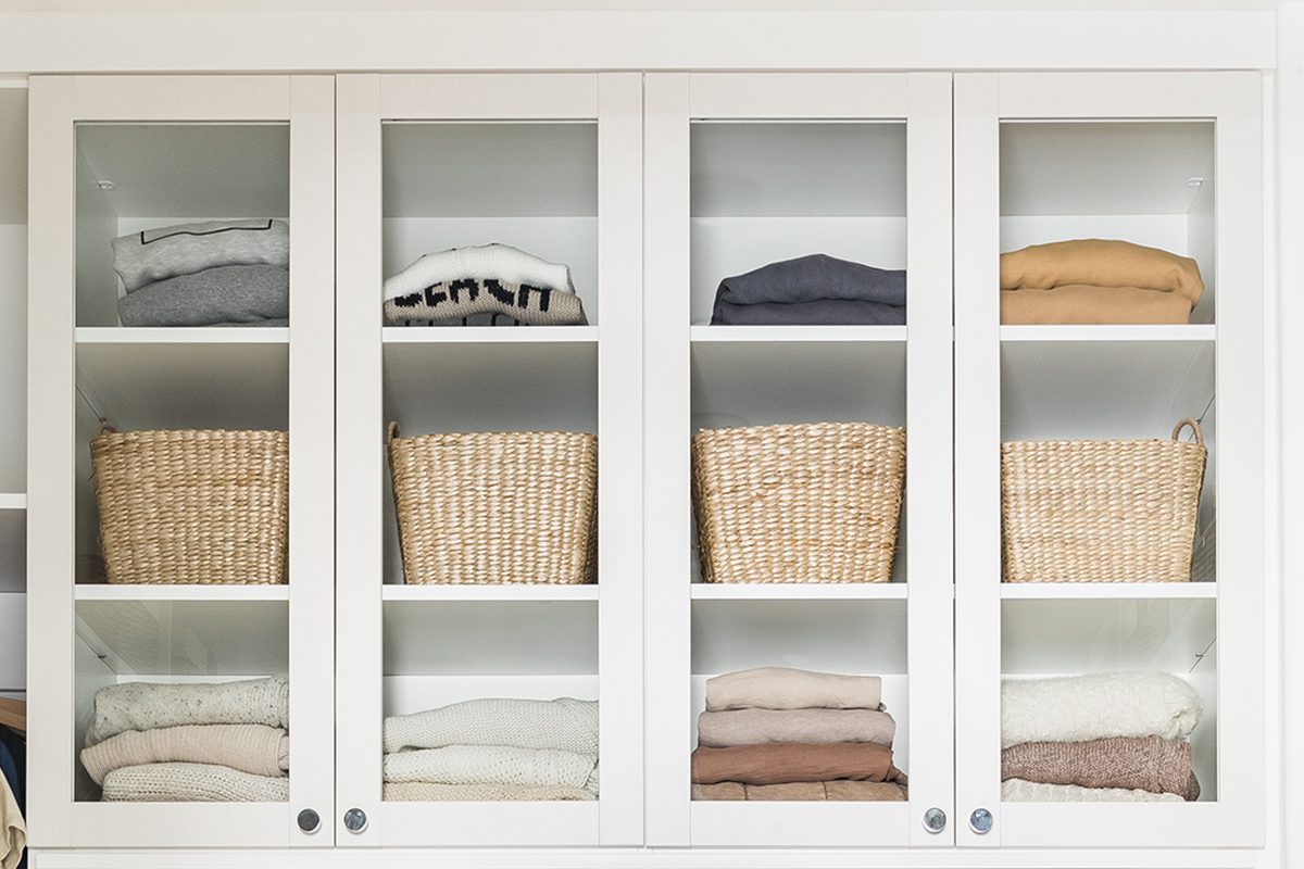 Las puertas de cristal del armario de ropa de cama del pasillo en acabado de madera veteada blanca de California Closets