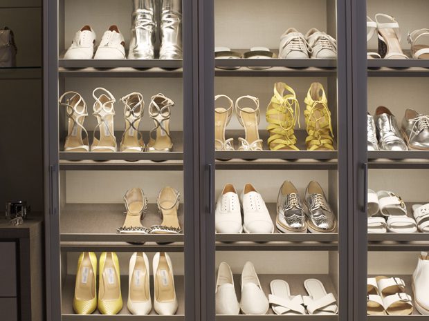 Shoe storage in a walk in closet with tilted shelving and LED lights to highlight contents created by California Closets