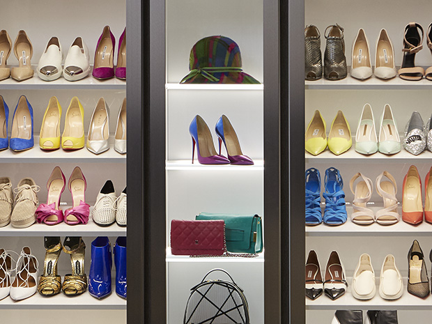 Shoes displayed on shelves in walk in closet with LED lighting and glass doors