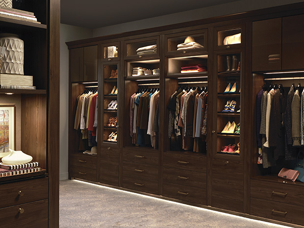 Walk in closet in dark brown wood grain finish with custom built in drawers, cabinets and open shelves created by California Closets