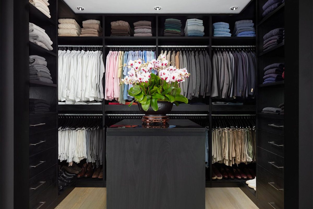 Dark wood finish walk in closet with open shelves, clothes hanging poles and center island created by California Closets