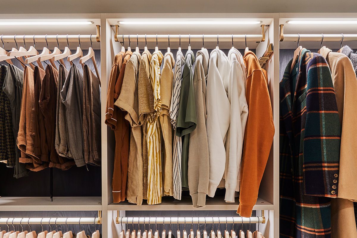Custom reach in closet showing clothes ordered by color and category with LED lighting feature created by California Closets