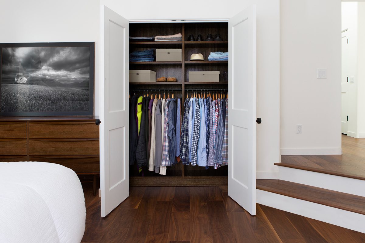 Small reach in closet for a bedroom with extra open shelving for storage in dark wood finish by California Closets