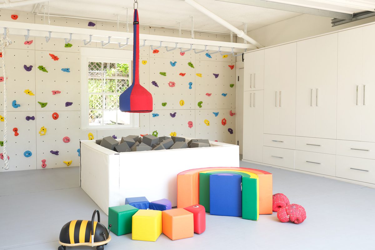 Playground designed for a converted garage with custom cabinets, shelving, climbing wall and jungle gym by California Closets