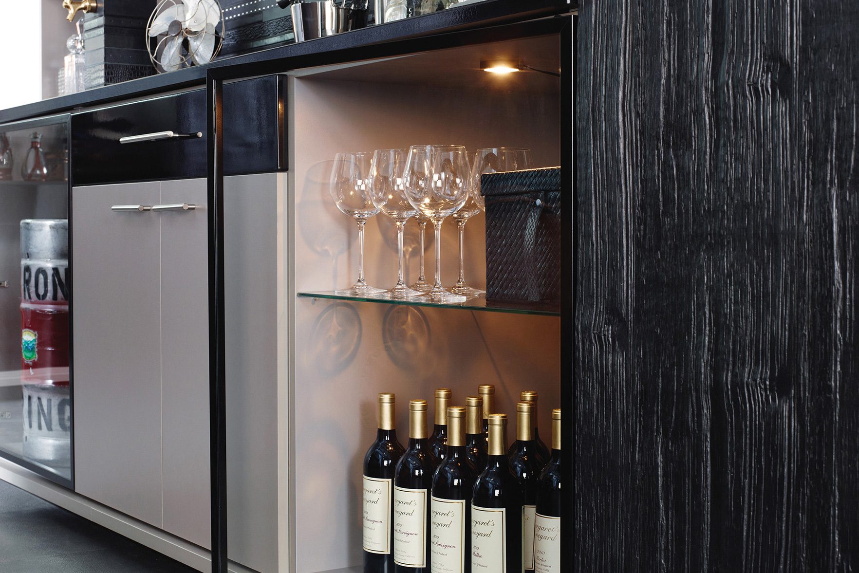 Wine bar in the home with open shelving, LED lighting, prep counter in dark wood grain finish by California Closets